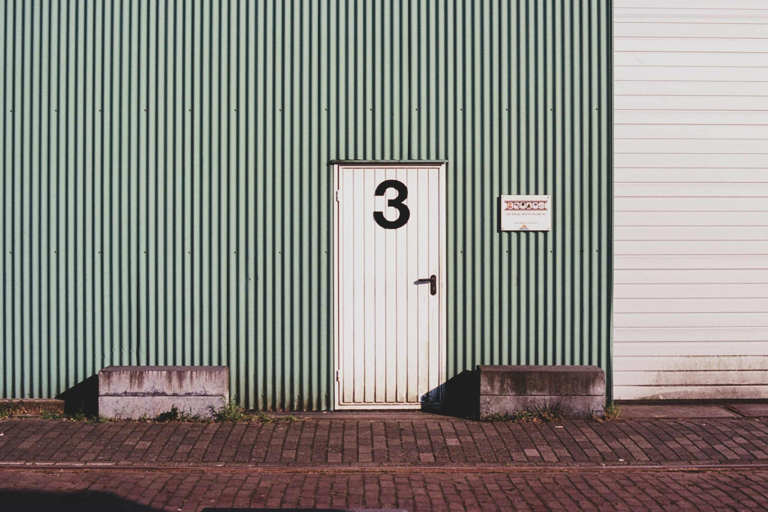 Green shed with a rocks infront of the building and a white door with the number 3 on the door